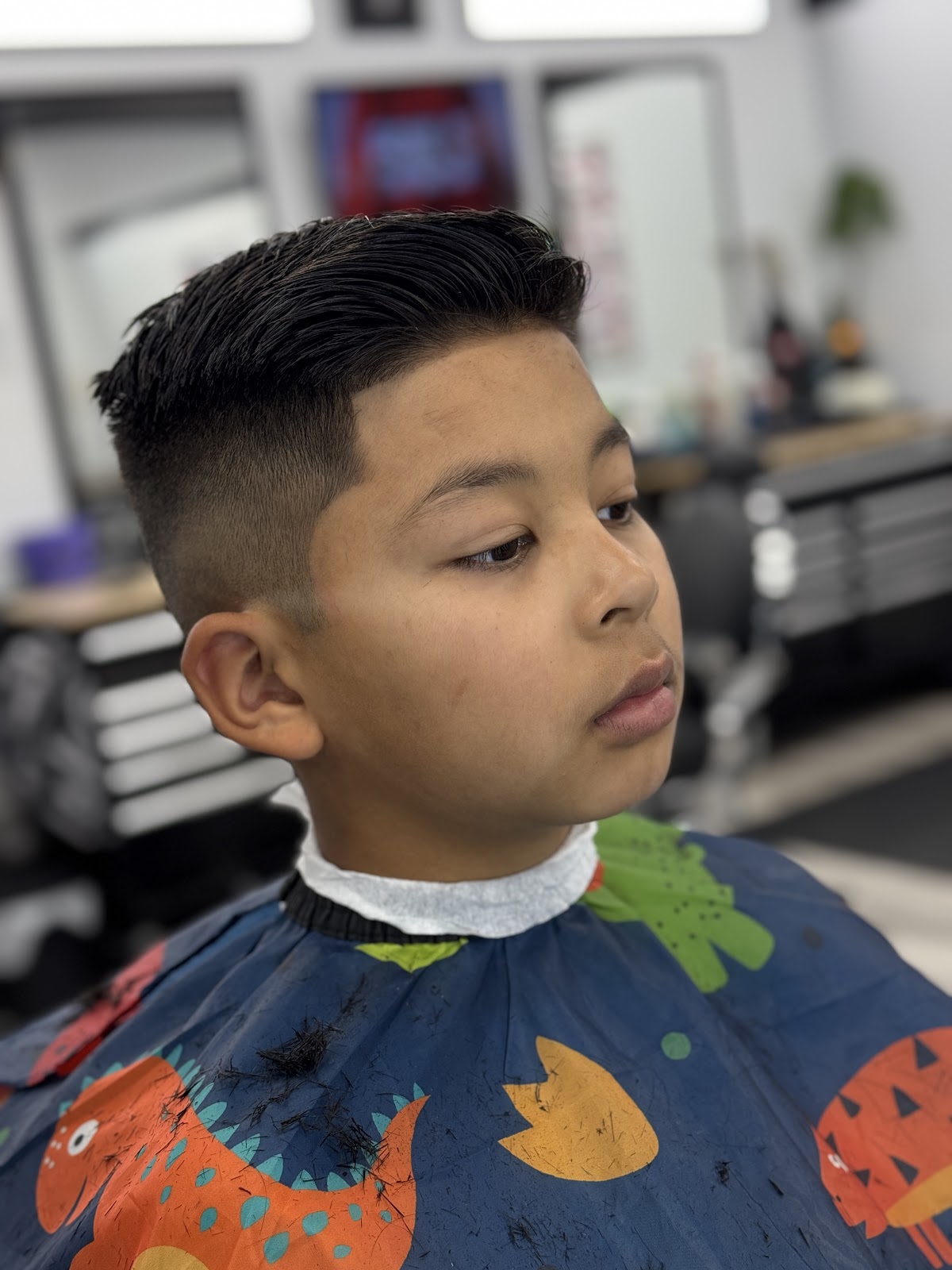 Kid's clean slick-back fade cut with shop interior behind